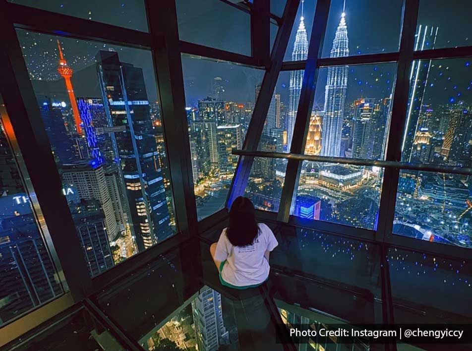 A woman seated on the floor of the Sky Deck at Imperial Lexis Kuala Lumpur, enjoying a view of the Petronas Twin Towers.