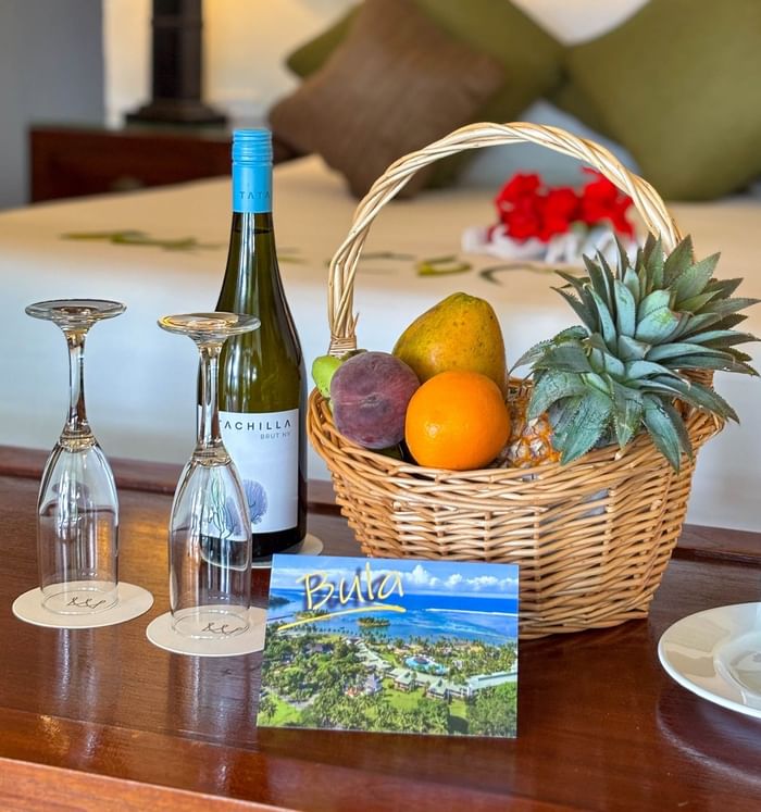 Bottle of wine, two glasses, and fruit basket on table at Naviti Resort Fiji Coral Coast