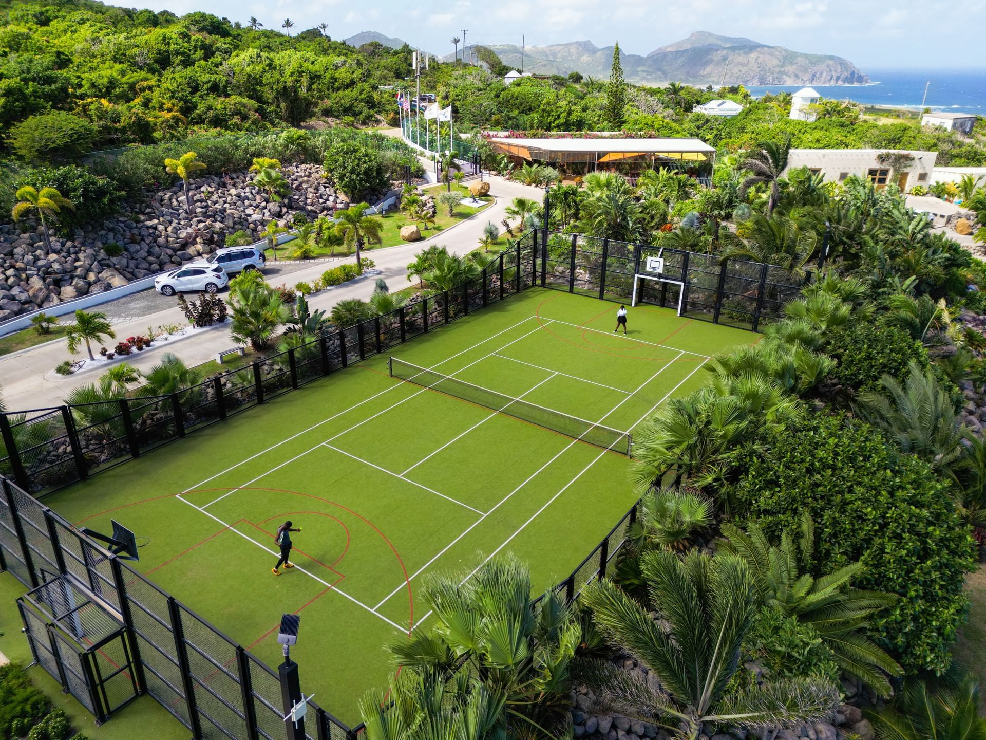 Aerial view of a multi-sport court surrounded by lush greenery, with a player practicing at Golden Rock Resort
