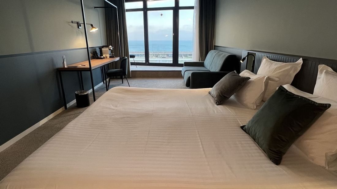 Chambre d'hôtel moderne avec grand lit, canapé, bureau et vue sur la mer.