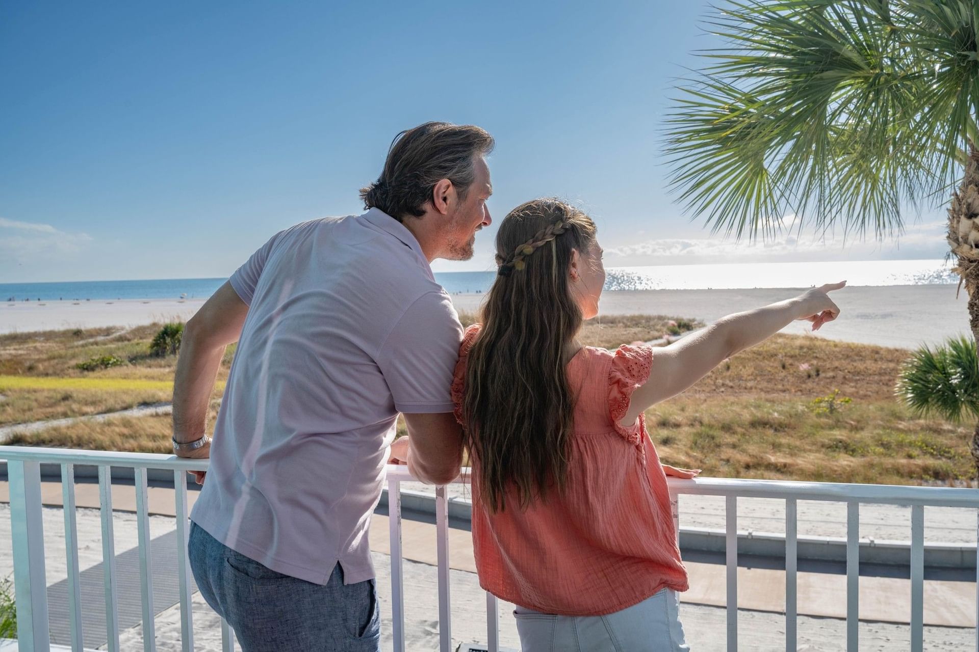 A couple is standing on a balcony overlooking the beach.