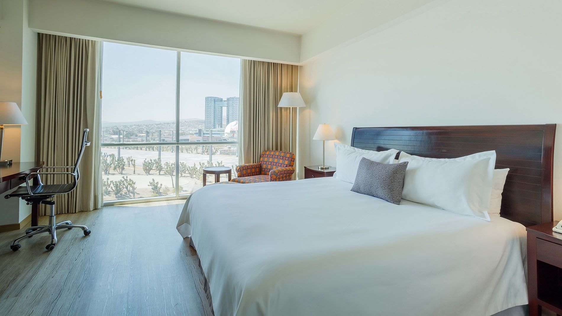 Sunlight King Camino Real Club with a king bed, and floor-to-ceiling windows showing the city at Camino Real Pachuca