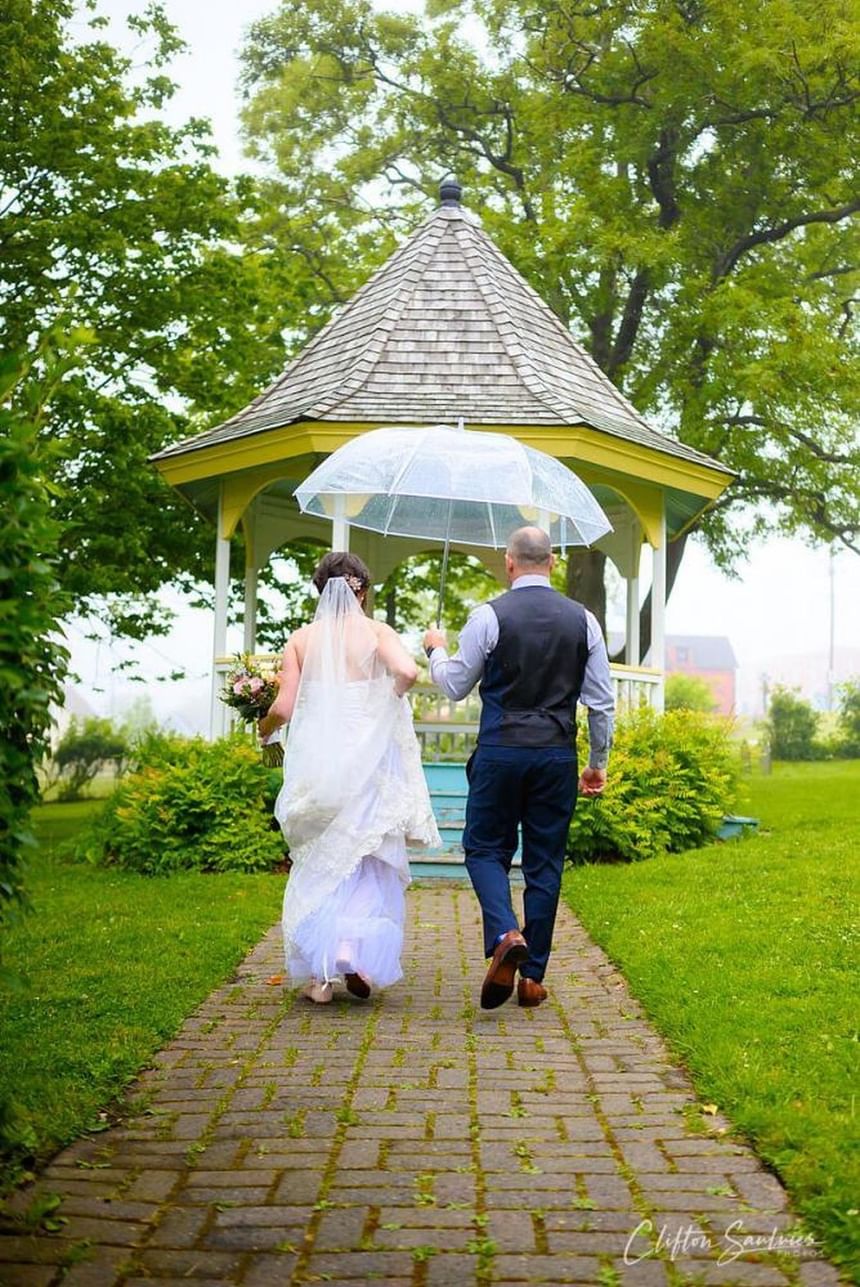 Bride and groom walking toward a garden gazebo, surrounded by lush greenery at Rodd Grand Yarmouth