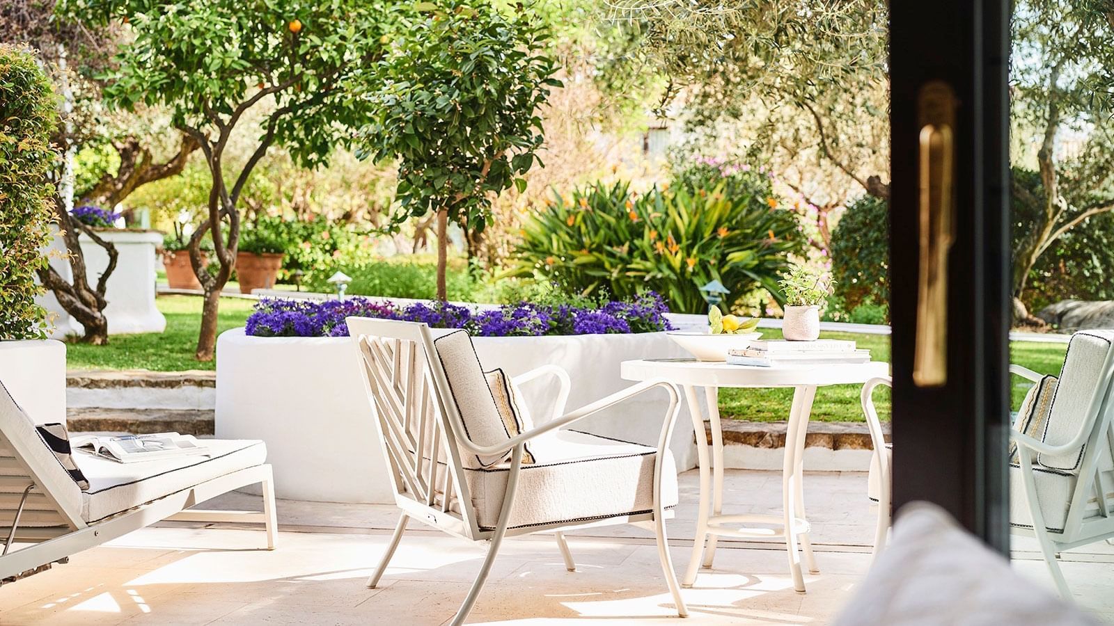 Junior Suite patio with lounge chairs and a table overlooking a garden filled with purple flowers at Marbella Club