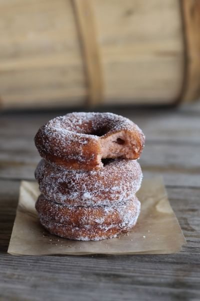 A stack of three sugar-coated donuts against a wooden backdrop. The top donut has a bite taken from it.