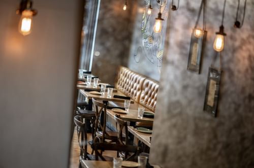 Leather booth by wooden tables and chairs under hanging Edison bulbs in BOTA at Warwick San Francisco