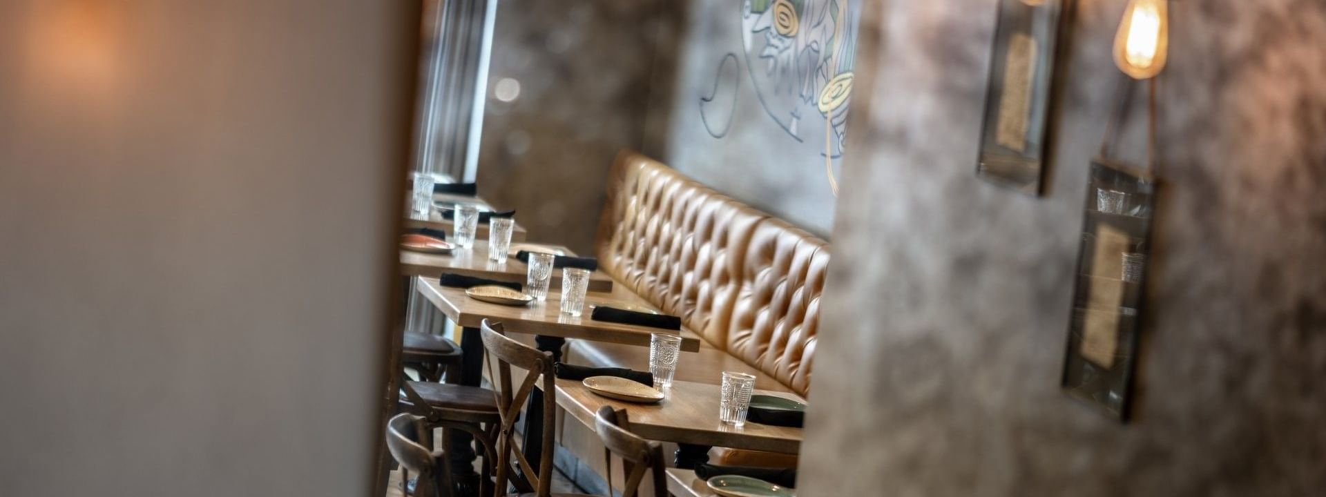 Leather booth by wooden tables and chairs under hanging Edison bulbs in BOTA at Warwick San Francisco
