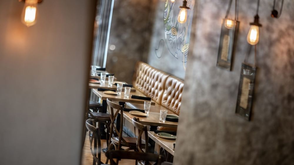 Leather booth by wooden tables and chairs under hanging Edison bulbs in BOTA at Warwick San Francisco