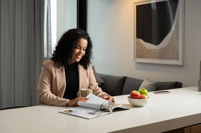 A lady reading a magazine with a drink at Nesuto Docklands
