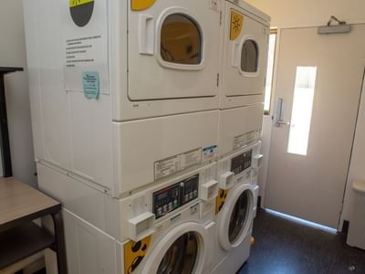 Four white stacked washers and dryers in a room at La Trobe University - Orde House.