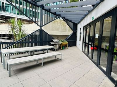 Outdoor seating area with tables and benches under a covered structure at UniLodge Auckland City.
