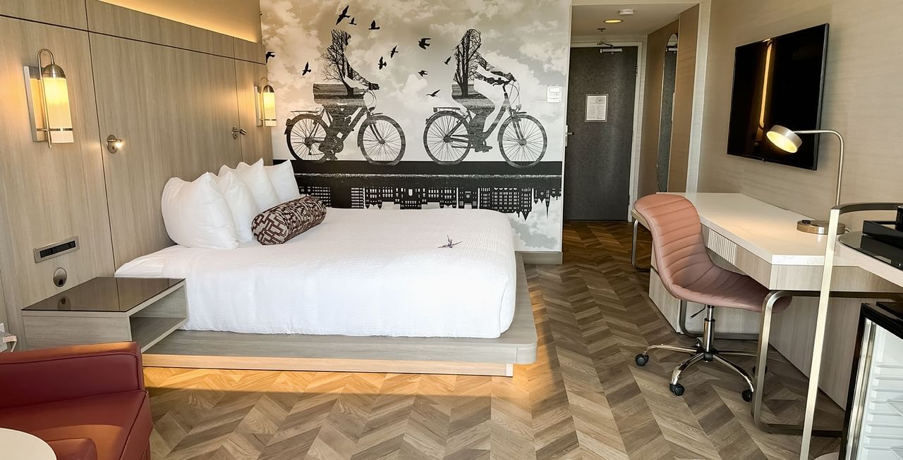 Hotel guestroom with king bed, work desk, chair, TV, and mini fridge