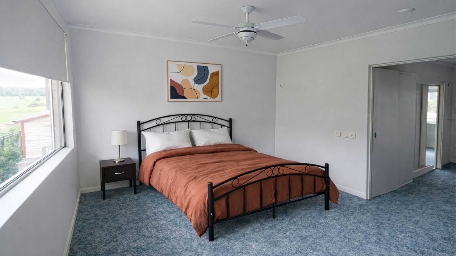 Bedroom with blue carpet, large window, bed, nightstand, and painting at UniLodge SCU Lismore - Sirius.