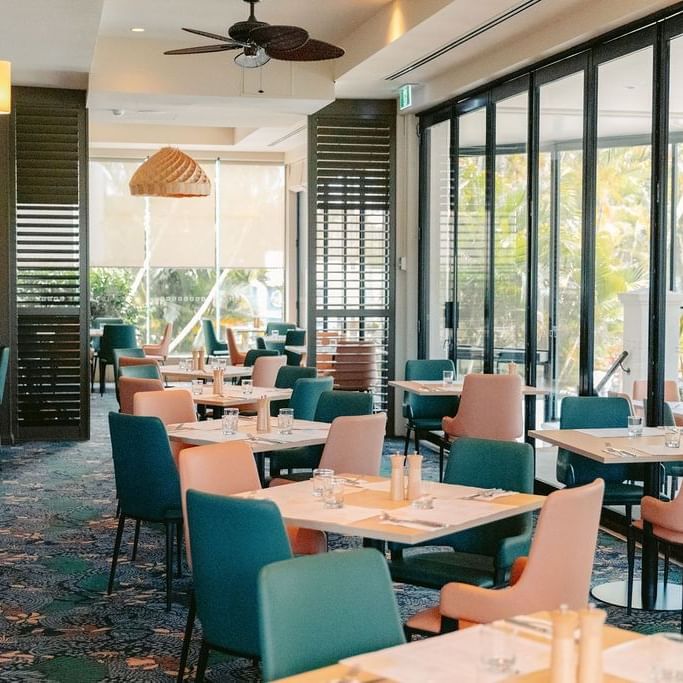 Modern restaurant interior with large glass windows, colorful chairs, and tables arranged in rows.