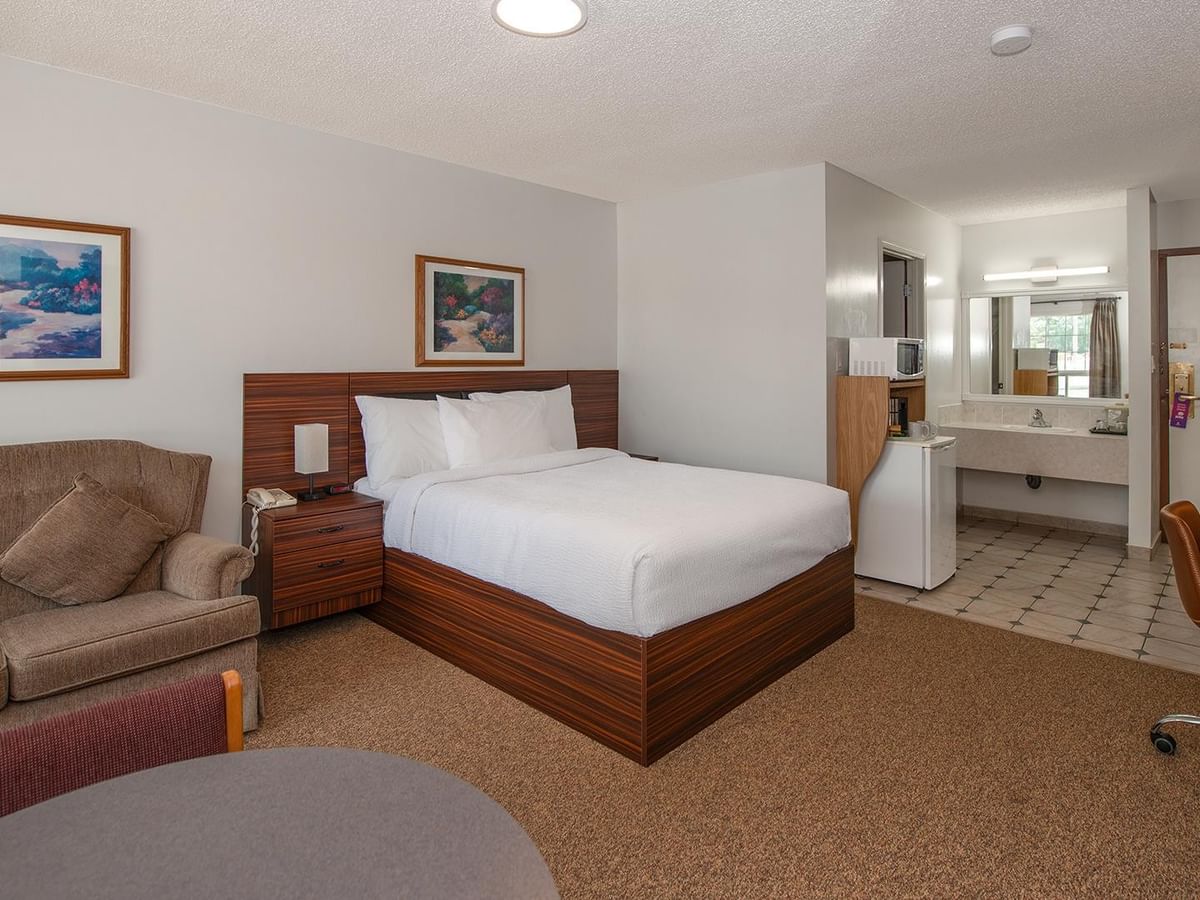 Spacious guest room with a queen bed, sofa, TV and open bathroom area.