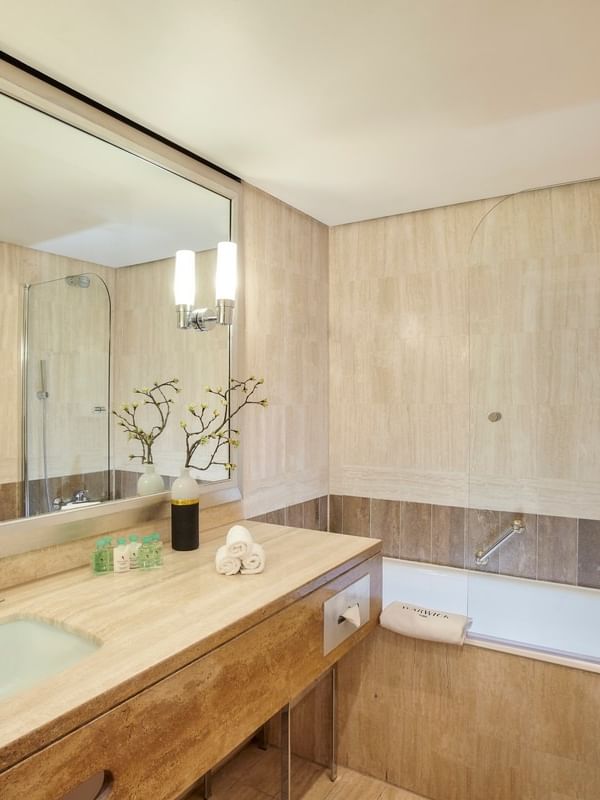 Beige stone vanity by a bathtub under a large mirror in Superior Room at Warwick Paris Champs Elysées