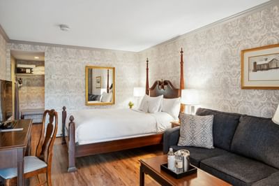 Four-poster bed beside sofa near wooden desk & mirror on wallpaper wall in the guest room at Avon Old Farms Hotel