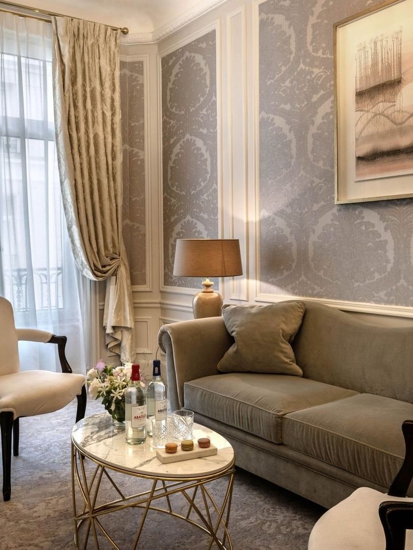 Living area with plush sofa under hanging wall art near window in Deluxe Suite Belle Époque atHotel Westminster Paris