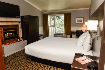 TV with fireplace and wardrobe facing the bed by the window in Deluxe King at Lake Natoma Inn