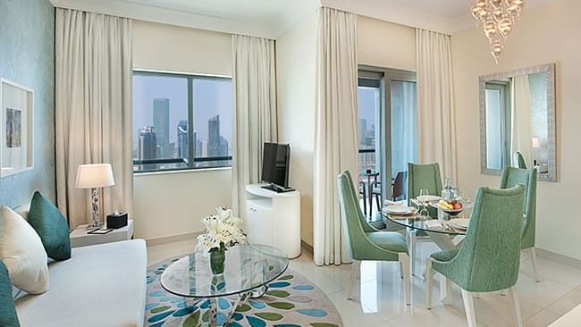 Lounge area with TV and dining table in Deluxe Room at DAMAC Maison Dubai Mall Street