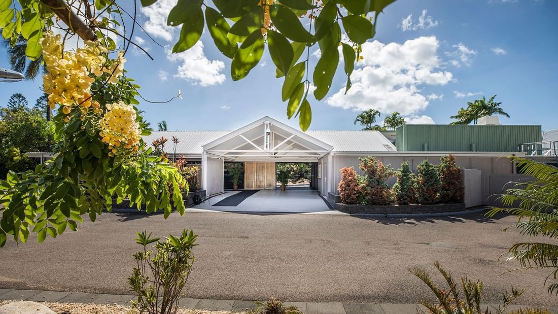 Ballroom Entrance, framed by lush green plants and flowers against a blue sky at Mercure Hotel Townsville