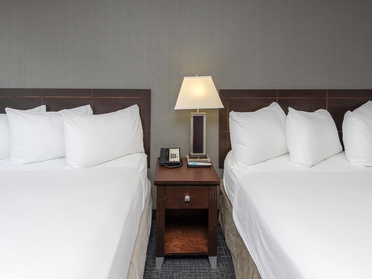 Two queen beds with white linens and pillows in a room.