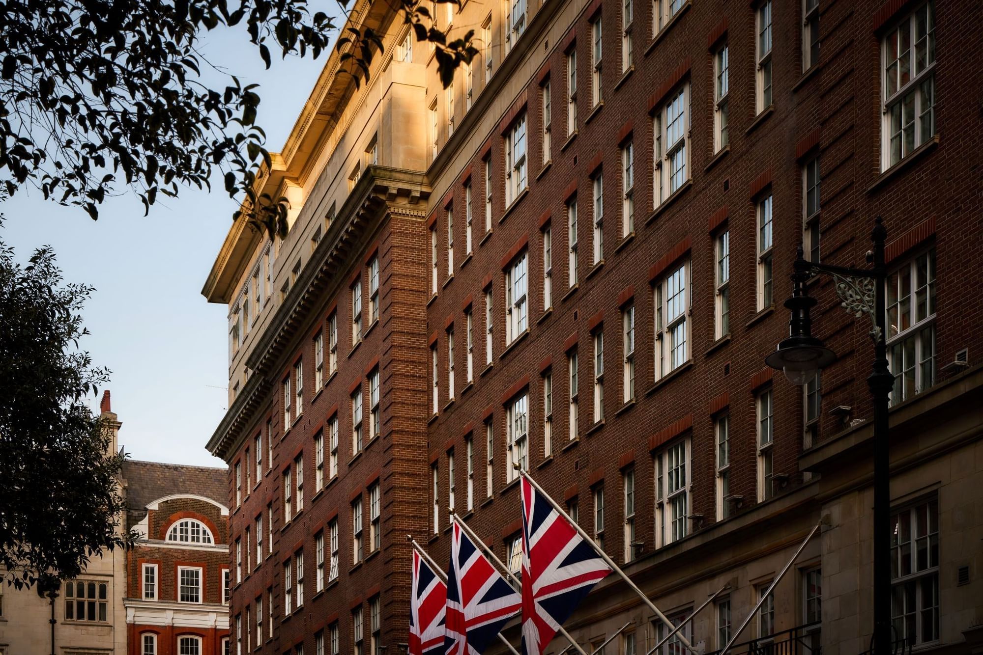 The May Fair Hotel, London with Union Jack flags in front of a brick facade. Exterior building of the May Fair Hotel.