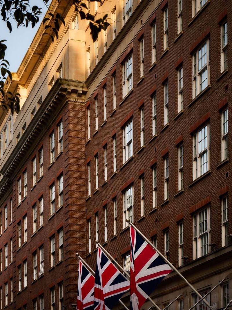 The May Fair Hotel, London with Union Jack flags in front of a brick facade. Exterior building of the May Fair Hotel.