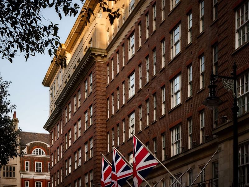 The May Fair Hotel, London with Union Jack flags in front of a brick facade. Exterior building of the May Fair Hotel.