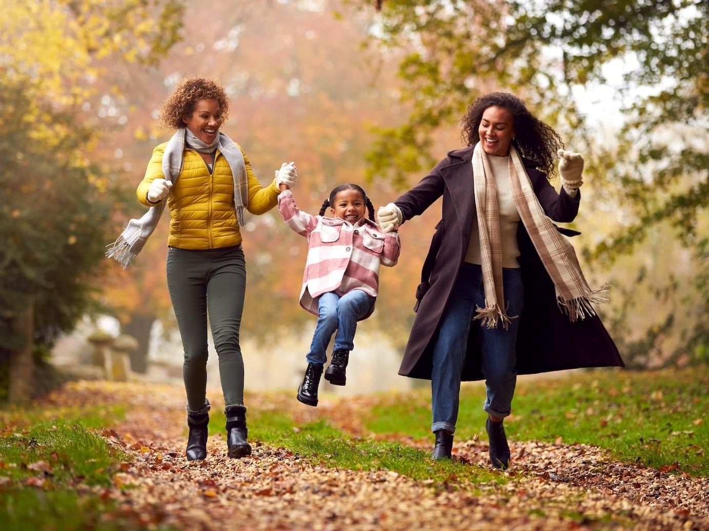 Two women and a child in winter clothing are walking and holding hands in a park.