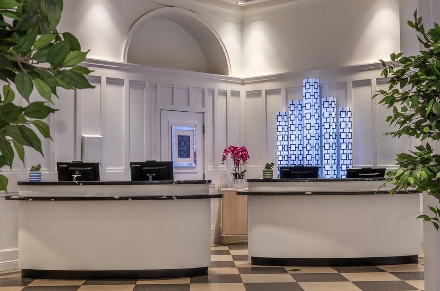 Reception desks placed by white paneled walls under decorative illuminated art at Warwick Allerton Chicago