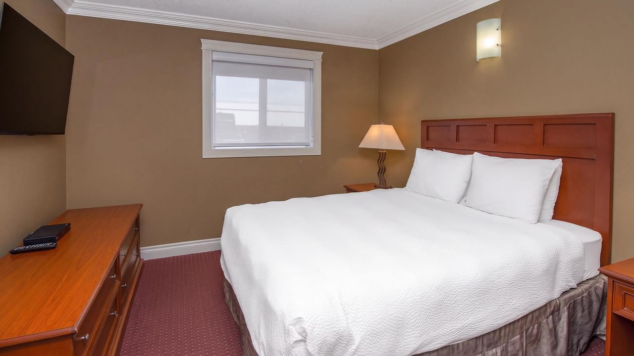 Guest room with white bedding, wooden headboard, and warm tan walls at Coast Edson Hotel.