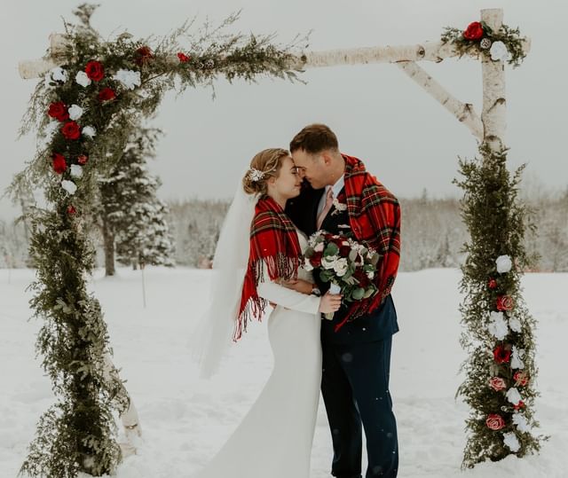 Bride and groom embracing under a rose-covered wooden arch, with falling snow at Mountain View Grand Resort & Spa