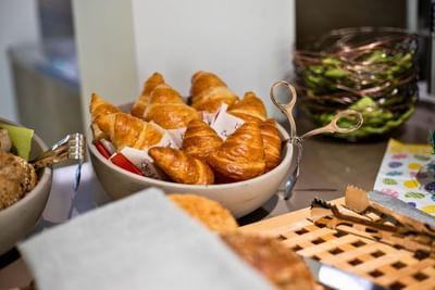 Bowl of croissants with paper wraps beside decorative utensils and pastries served at Avaneo Hotel Marktredwitz