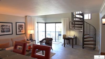 Living area with a sofa and armchair near glass balcony doors and a spiral staircase in Governors Lanai at Miami Lakes Hotel