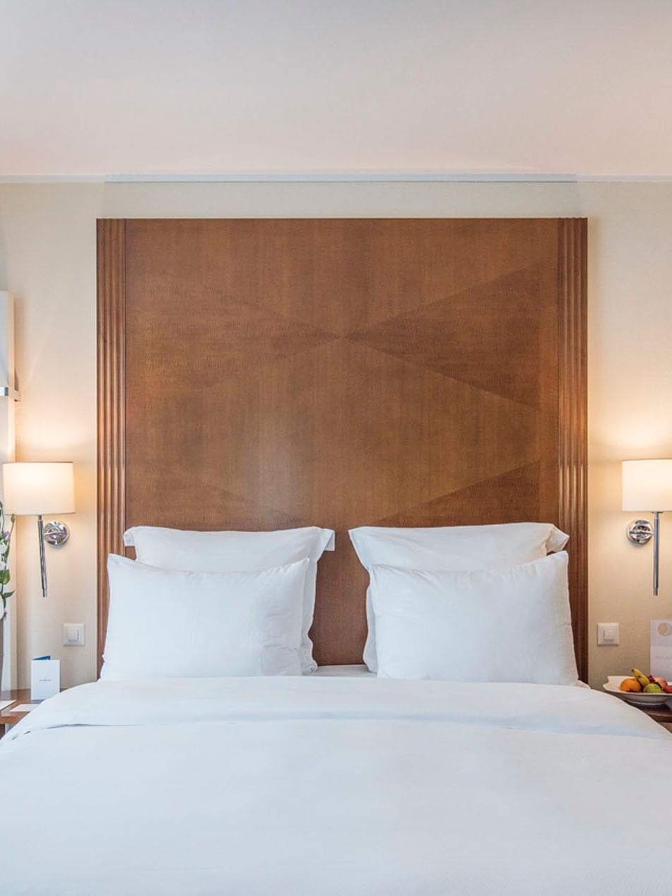 King bed with a wood headboard by small side tables under glowing wall lamps in Classic Room at Warwick Geneva
