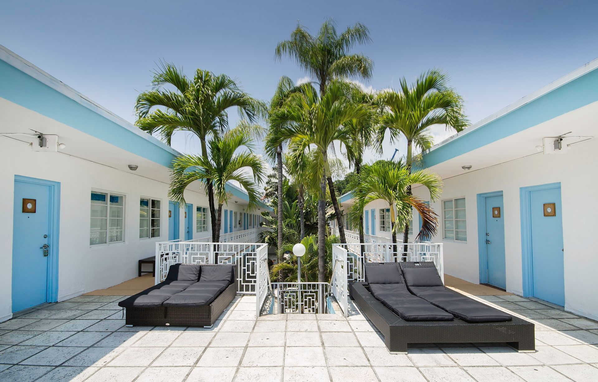 A courtyard with lounge chairs, palm trees, and a white and blue building