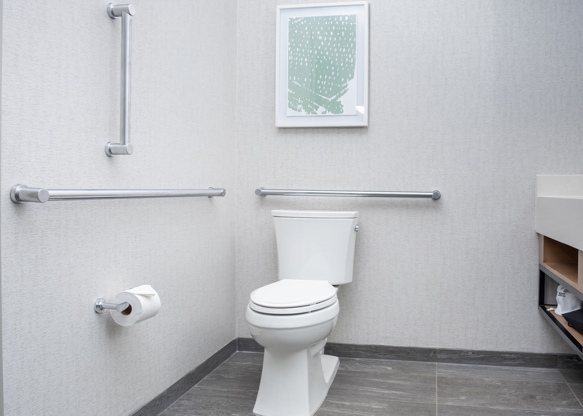 A clean and modern bathroom with a white toilet, gray tile floor, and grab bars.
