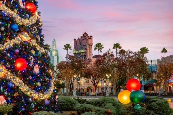 A large Christmas tree in Hollywood Studios with the Tower of Terror and other theme park attractions in the background.