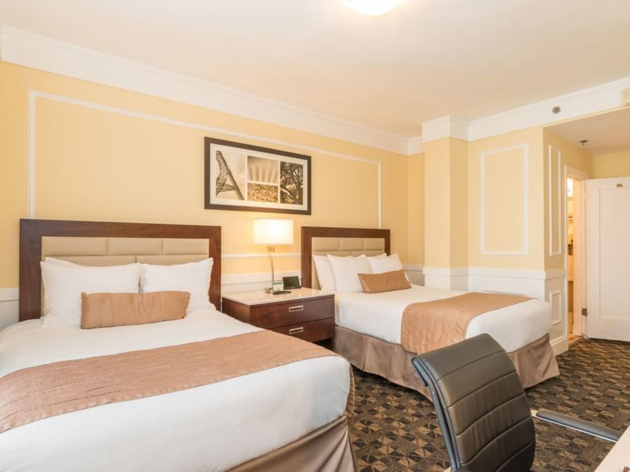 Two beds, nightstand, lamp, and chair in a yellow-themed hotel room at Pickwick San Francisco.
