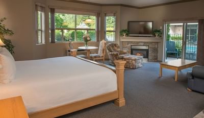Bed near a stone fireplace, patio doors open to the lush outdoor setting in Hilltop Suite at Hilltop Inn, Salmon Arm