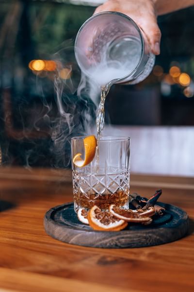 Hand pouring a steamy liquid into a glass with dried citrus served in a restaurant at El Mangroove Hotel