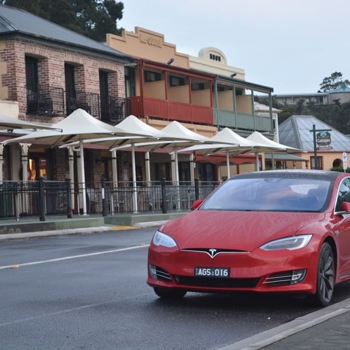 Red Tesla Electric car driving on the road near Strahan Village