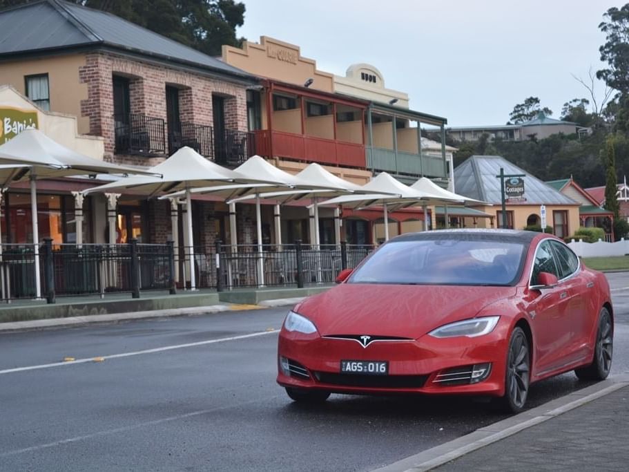 Red Tesla Electric car driving on the road near Strahan Village