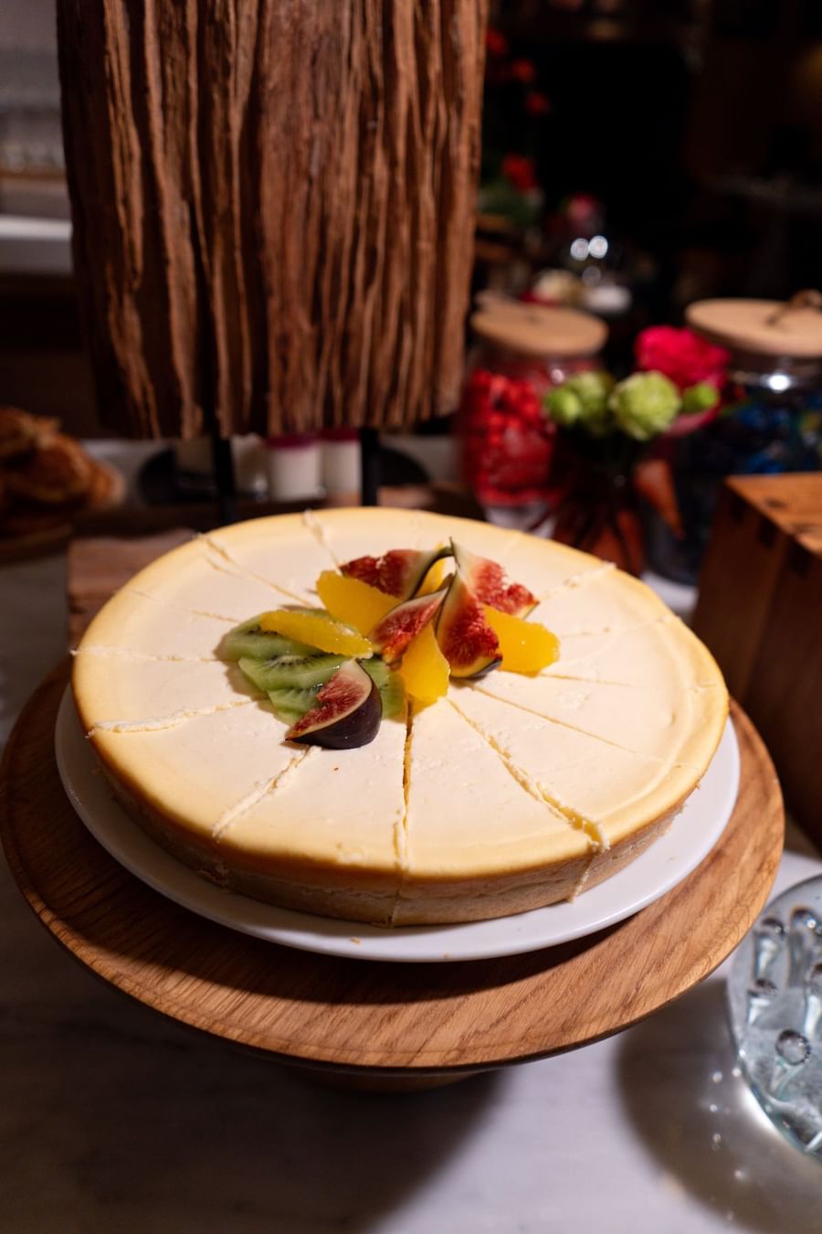 Une part de cheesecake garnie de figues fraîches, de kiwis et d'oranges, posée sur une table au Warwick Paris Champs-Élysées