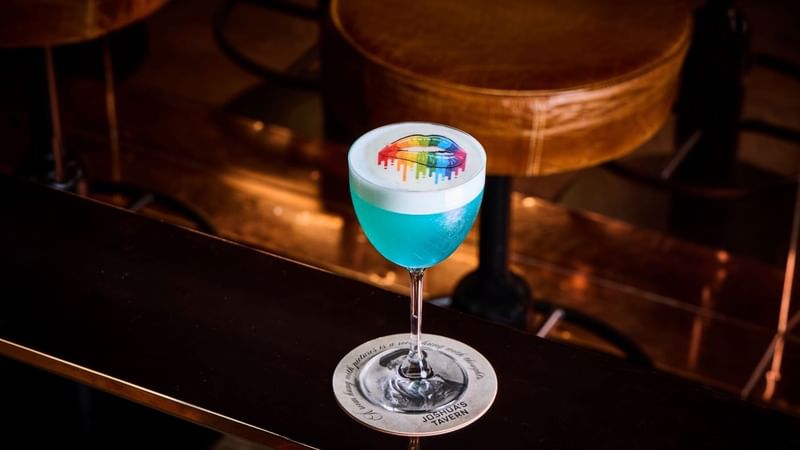 Blue Pride cocktail with rainbow lips design on bar counter at Joshida's Tavern.