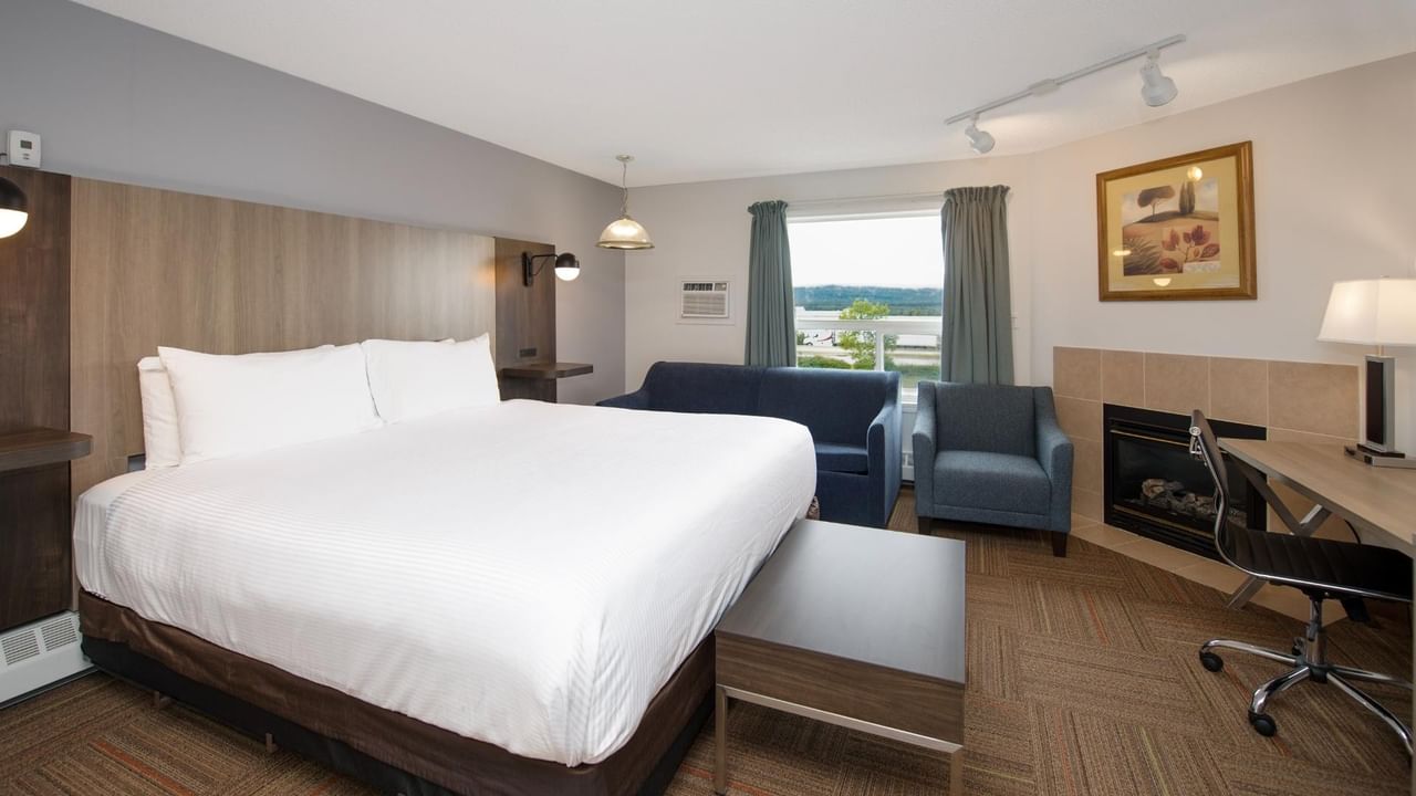Hotel room with bed, couch, desk, chair, fireplace, and window with curtains.