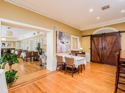 Dining tables by a wooden barn door, under recessed lights near potted plants and an oil painting at Simsbury 1820 House