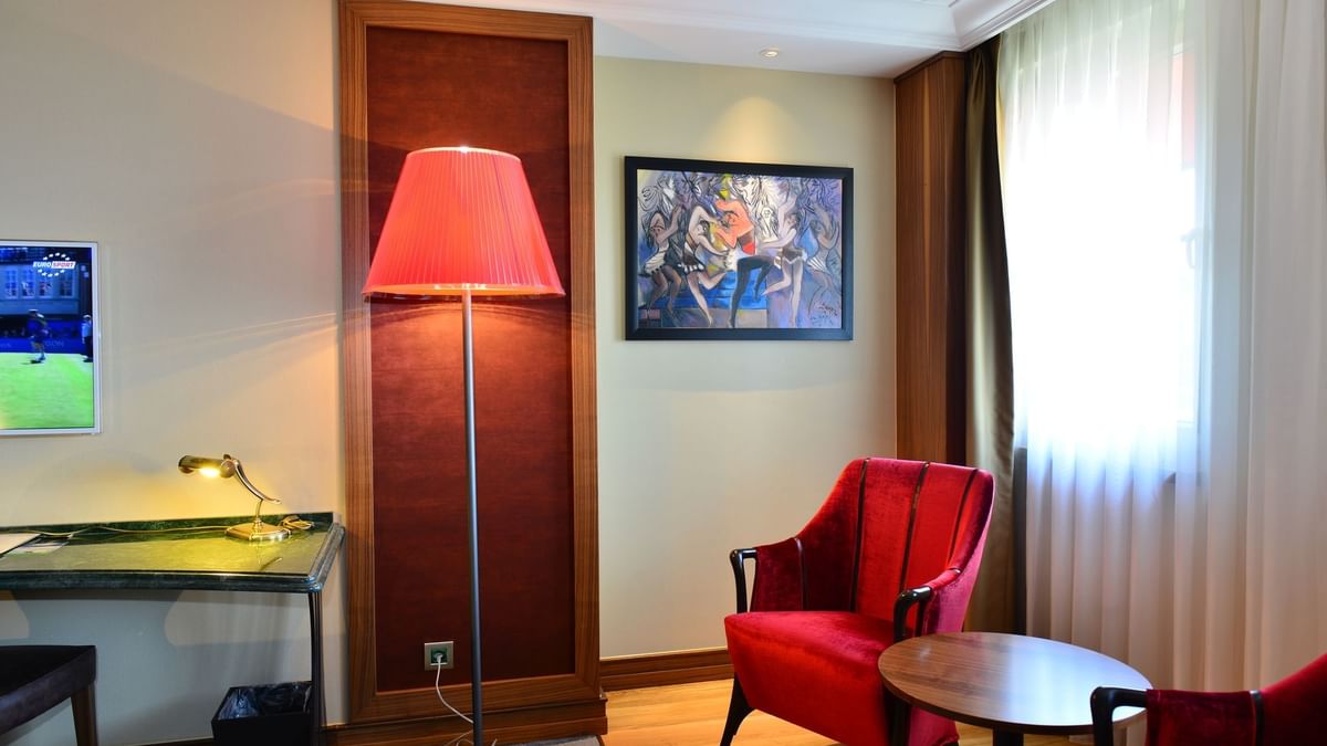 Elegantly furnished Deluxe Room with Tall red lamp by a velvet chair surrounding a small wooden table at Warwick Ankara