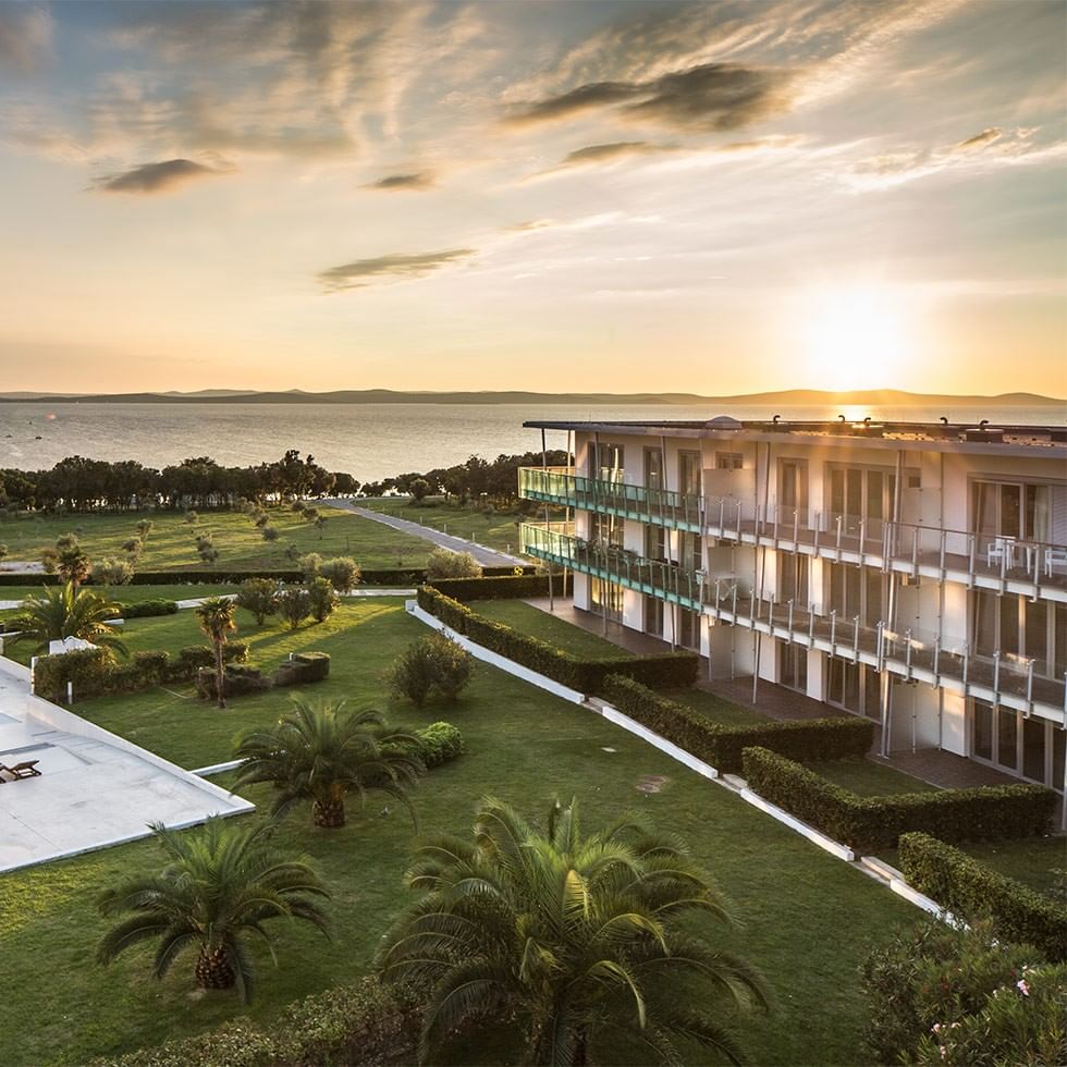 Tramonto su un resort con piscina, palme, e vista sull'oceano.